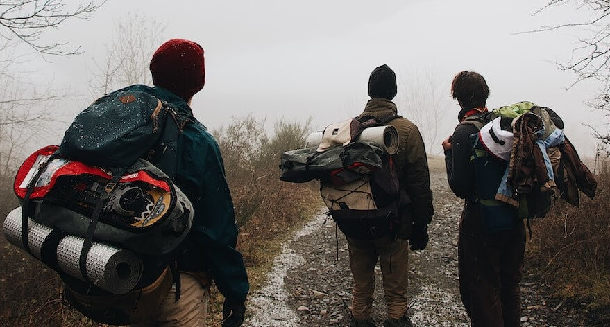 Three hikers with backpacks, featuring attached clothes and jackets for easy access and storage during the trek.