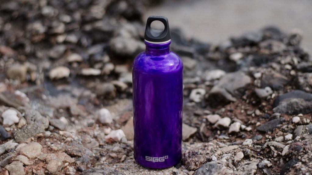 Purple metal water bottle placed on rocky ground.